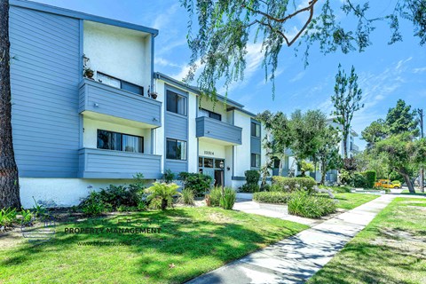 a white and grey apartment building with a sidewalk in front of it